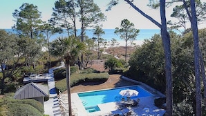 A pool area with a view of the beach, surrounded by trees and a small building. - Oceanfront Sea Pines Home w/ Pool (Hilton Head Island)