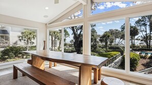 A spacious room with a large table and bench, large windows offering a view of a landscaped garden and pool. - Oceanfront Sea Pines Home w/ Pool (Hilton Head Island)