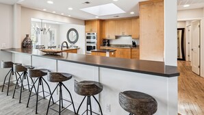 A modern kitchen with a central island, wooden cabinets, and a large window. - Oceanfront Sea Pines Home w/ Pool (Hilton Head Island)