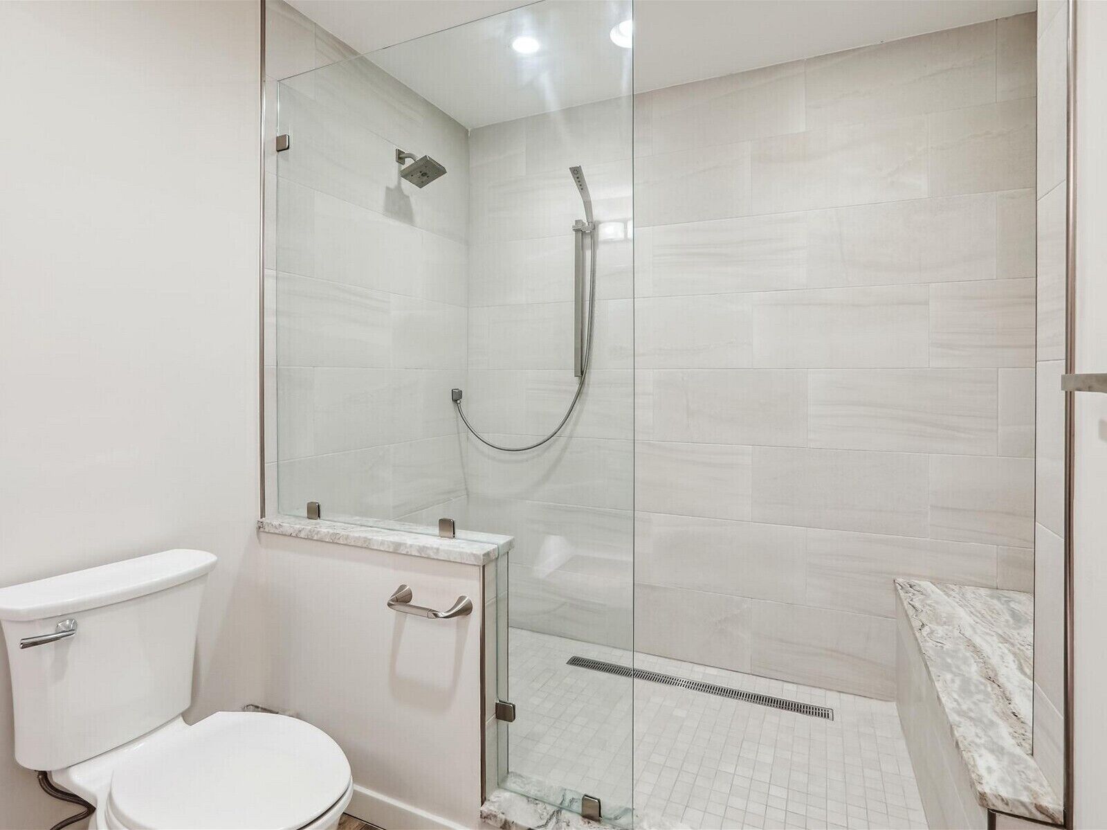 A modern bathroom with a glass-enclosed shower, a toilet, and a marble countertop.