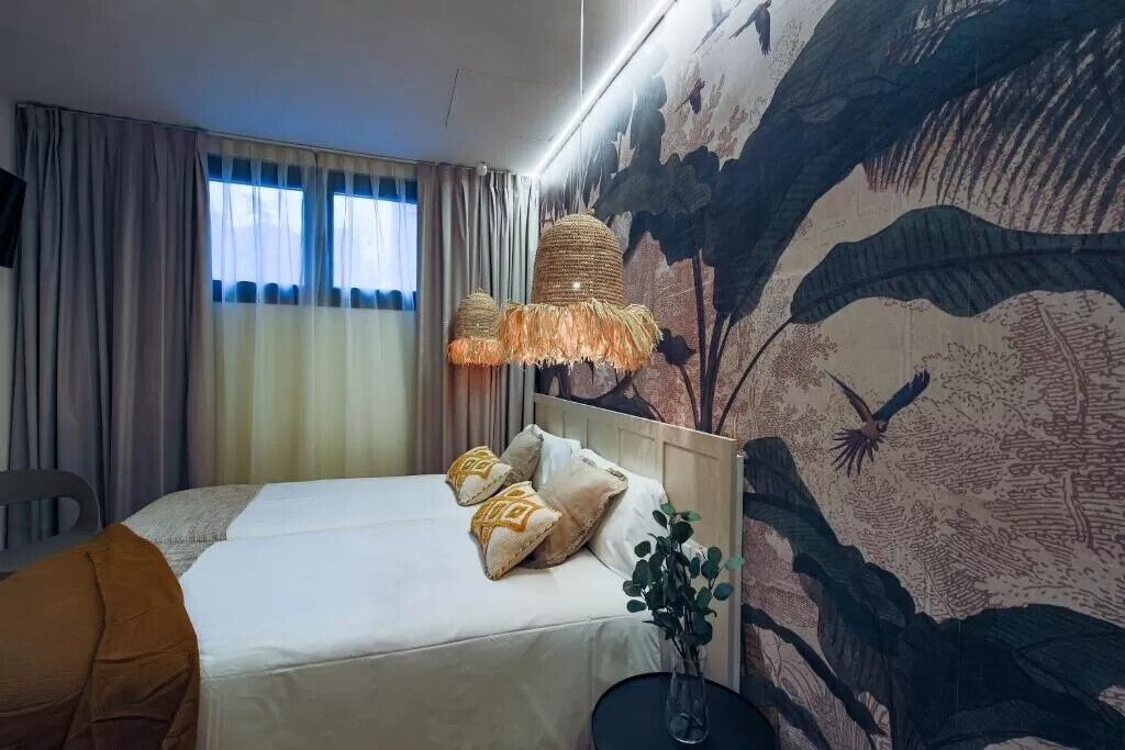 A hotel room with a bed, curtains, a wall mural, and a hanging lamp.