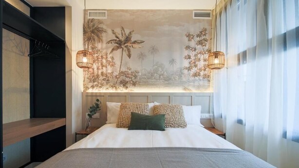 Una cama bien hecha con una colcha estampada, dos almohadas decorativas y un cabecero con un mural floral.
