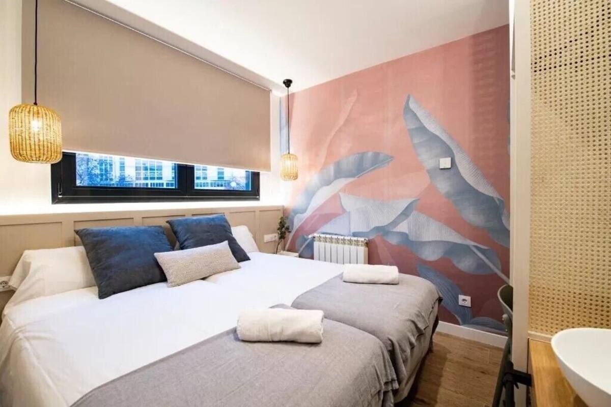 A modern bedroom with a large bed, two bedside tables, a window with a view, and a decorative wall mural.