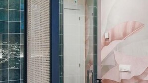 Un baño con un amplio box de ducha de vidrio, un lavabo blanco sobre encimera de madera y una pared decorada con un mural floral.