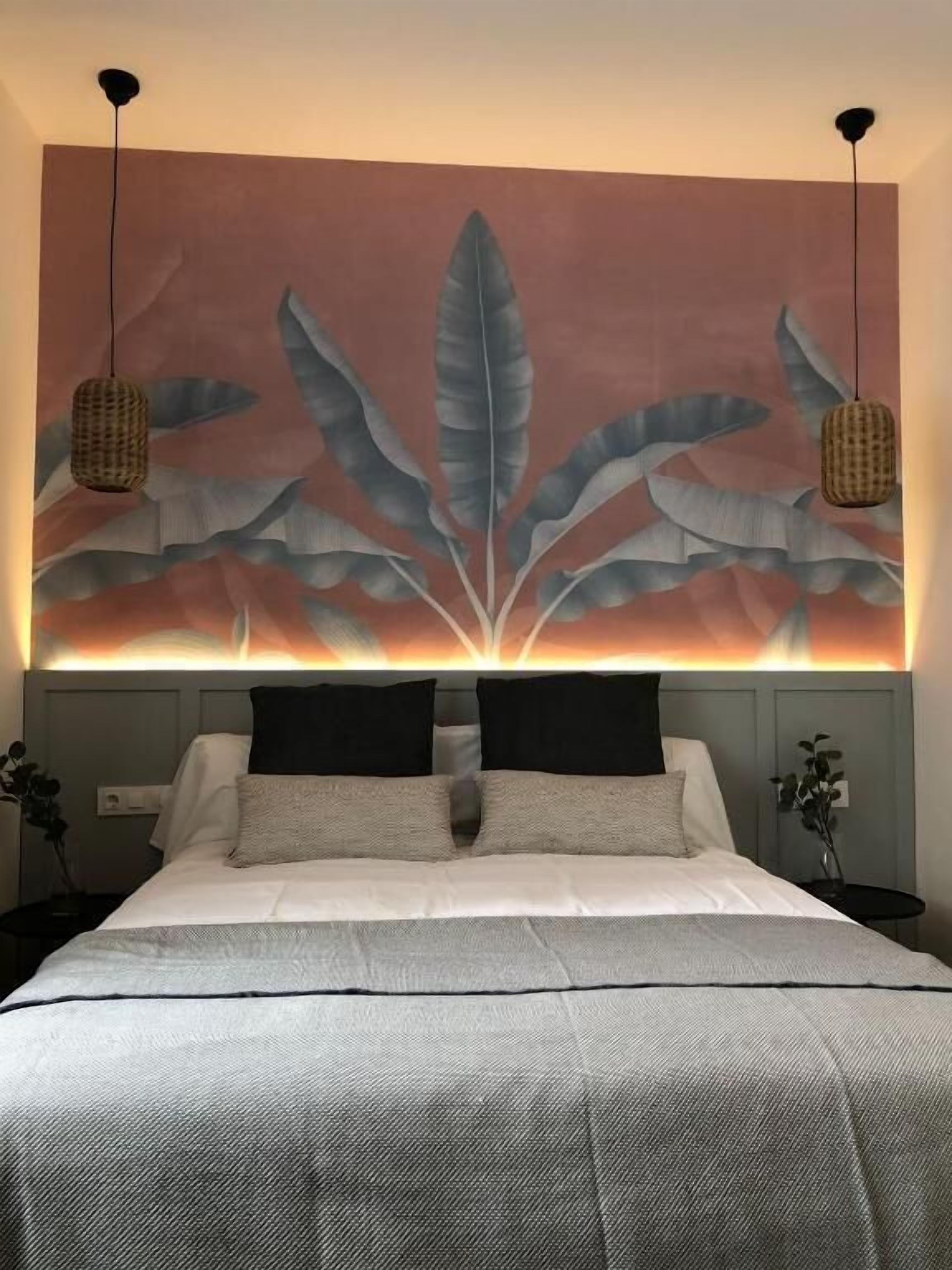 A bed with a headboard featuring a large, abstract leaf design. There are two hanging lamps on either side of the bed.