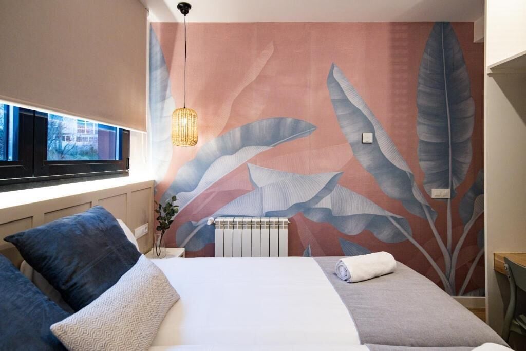 A hotel room with a large bed, a window with a view, a radiator, and a wall with a leaf pattern.