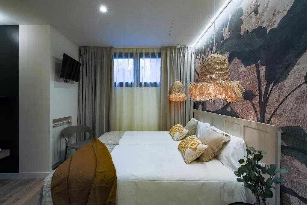 A hotel room with a bed, a TV mounted on the wall, a window with curtains, and a wall mural.