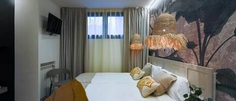 A hotel room with a bed, a TV mounted on the wall, a window with curtains, and a wall mural.
