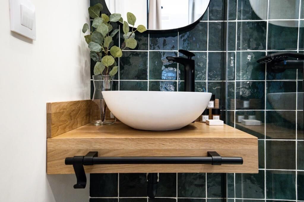 Un baño con tocador de madera, un lavamanos tipo cuenco blanco, un grifo negro y un espejo sobre el lavamanos.