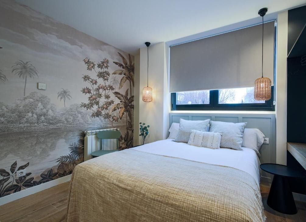 A bedroom with a large bed, a window with a view, a wall mural, and a hanging light fixture.