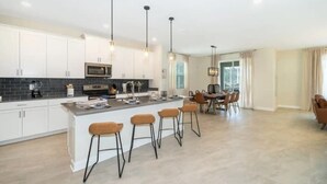 A modern kitchen with white cabinets, a central island with bar stools, and pendant lighting. - Family home w/private pool & hot tub near Disney (Kissimmee)