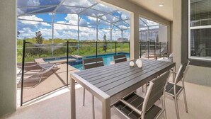 An outdoor patio with a table and chairs, a glass enclosure, and a view of a swimming pool. - Family home w/private pool & hot tub near Disney (Kissimmee)