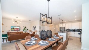 A modern dining area with a wooden table set for four, surrounded by brown chairs. A large, textured vase is placed on the table. - Family home w/private pool & hot tub near Disney (Kissimmee)