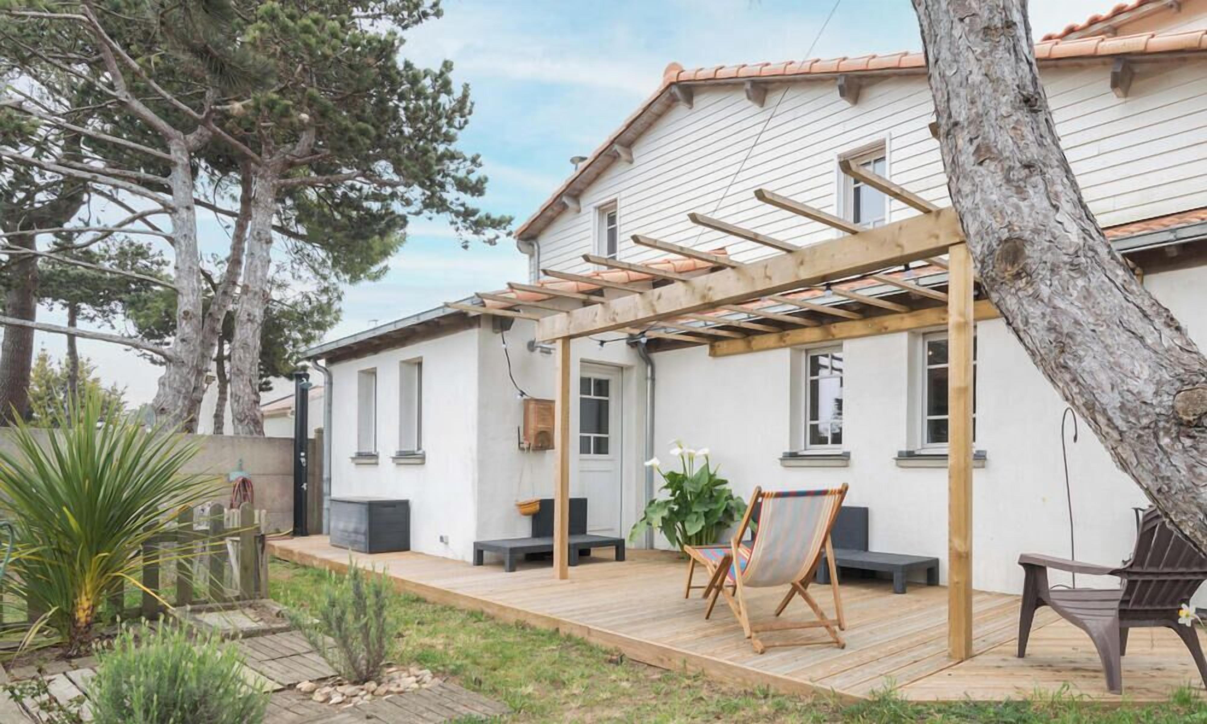 A house with a wooden deck, a pergola, and outdoor seating.