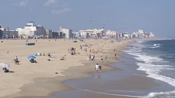 A beach with buildings in the background and people enjoying the sand and water.