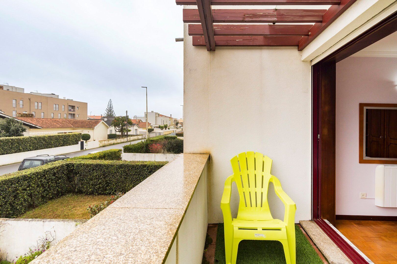 A balcony with a yellow chair, a view of the street, and a building in the background.
