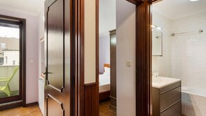 A hotel room with a wooden door, a bathroom with a white sink and mirror, and a view of the outside balcony. - GuestReady - Comfortable Retreat in Esposende (Esposende)