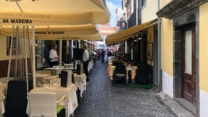 A narrow cobblestone street lined with outdoor dining tables and umbrellas, suggesting a restaurant or café setting. - Costa's Old Town House (Funchal)