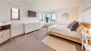 A bedroom with a bed, dresser, TV, windows, and a view of the sea. - 5 bedroom accommodation in Berwick-Upon-Tweed (Berwick-Upon-Tweed)