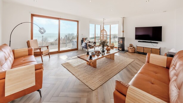 A spacious living room with a large TV, a fireplace, and a view of the sea through large windows. - 5 bedroom accommodation in Berwick-Upon-Tweed (Berwick-Upon-Tweed)