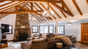 Ein geräumiges Wohnzimmer mit Kamin aus Stein, Holzbalken und einem großen Ecksofa.
