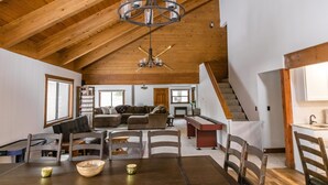 Ein geräumiger Wohnbereich mit hoher Decke, Holzbalken, einem Esstisch mit Stühlen, einer Couch und einer Treppe, die in ein Obergeschoss führt.