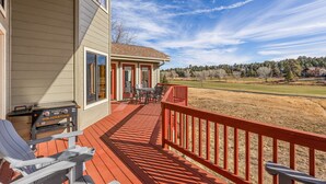 A deck with a red railing, a grill, and a table with chairs.