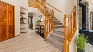 A spacious living area with a wooden staircase, a stone fireplace, and a large wooden door.