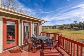 Une véranda avec une table et des chaises, une balustrade rouge et une vue sur un paysage verdoyant.