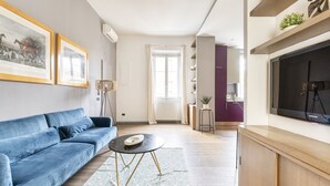 A modern living room with a blue sofa, a round coffee table, and a flat-screen TV. - Art Apartment Boboli Suite A few step from Porta Romana and Boboli's garden (Firenze)