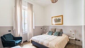 A bedroom with a bed, a chair, a bedside table with a lamp, a framed picture on the wall, and a window with curtains. - Art Apartment Boboli Suite A few step from Porta Romana and Boboli's garden (Firenze)