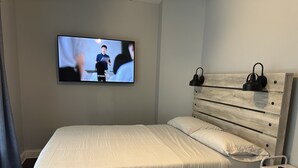 Un dormitorio con una cama, un televisor montado en la pared y un cabecero de madera.