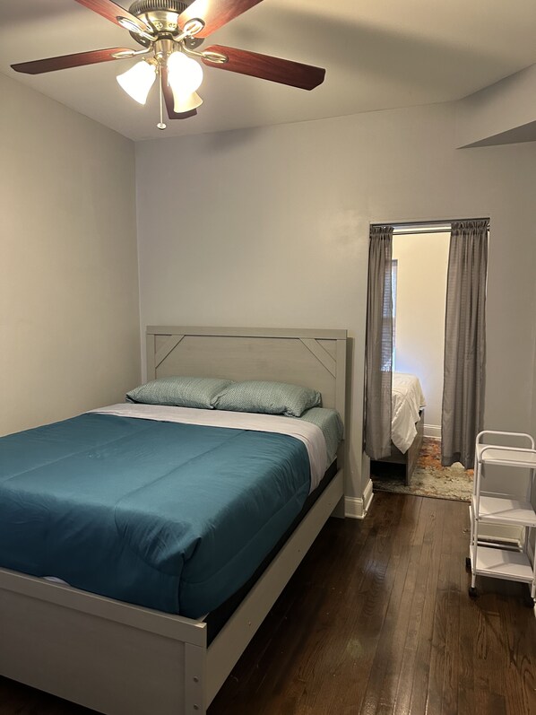 A bedroom with a bed, a ceiling fan, a nightstand, and a door leading to another room.