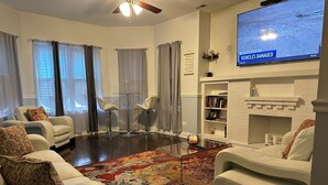 Una sala moderna con chimenea, sofás de cuero, una mesa de centro y un televisor de pantalla plana mostrando un noticiero.