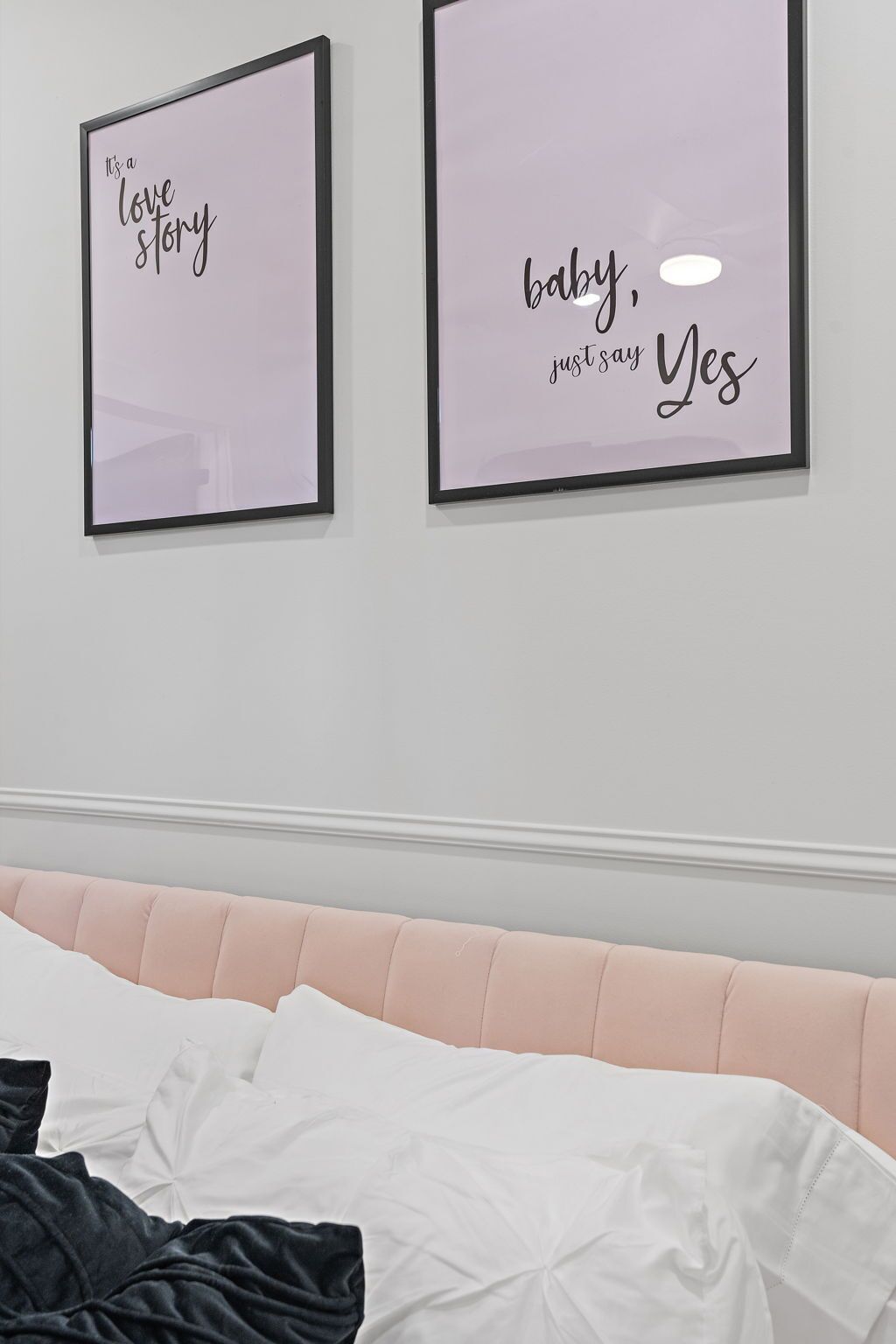 Een slaapkamer met een roze hoofdbord, witte beddengoed en twee ingelijste posters aan de muur.