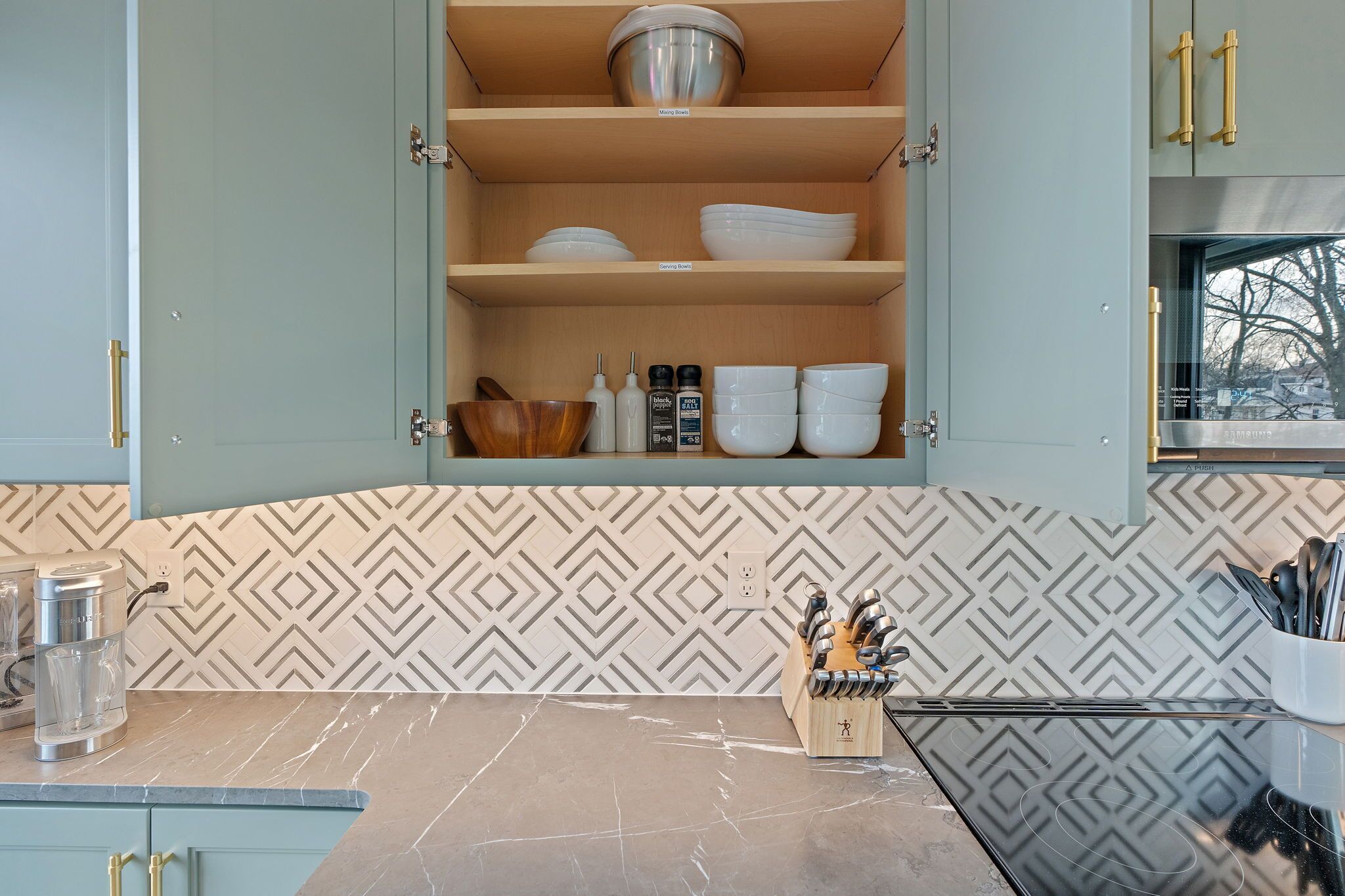 A kitchen with a patterned backsplash, a countertop with a water dispenser, and a knife block.