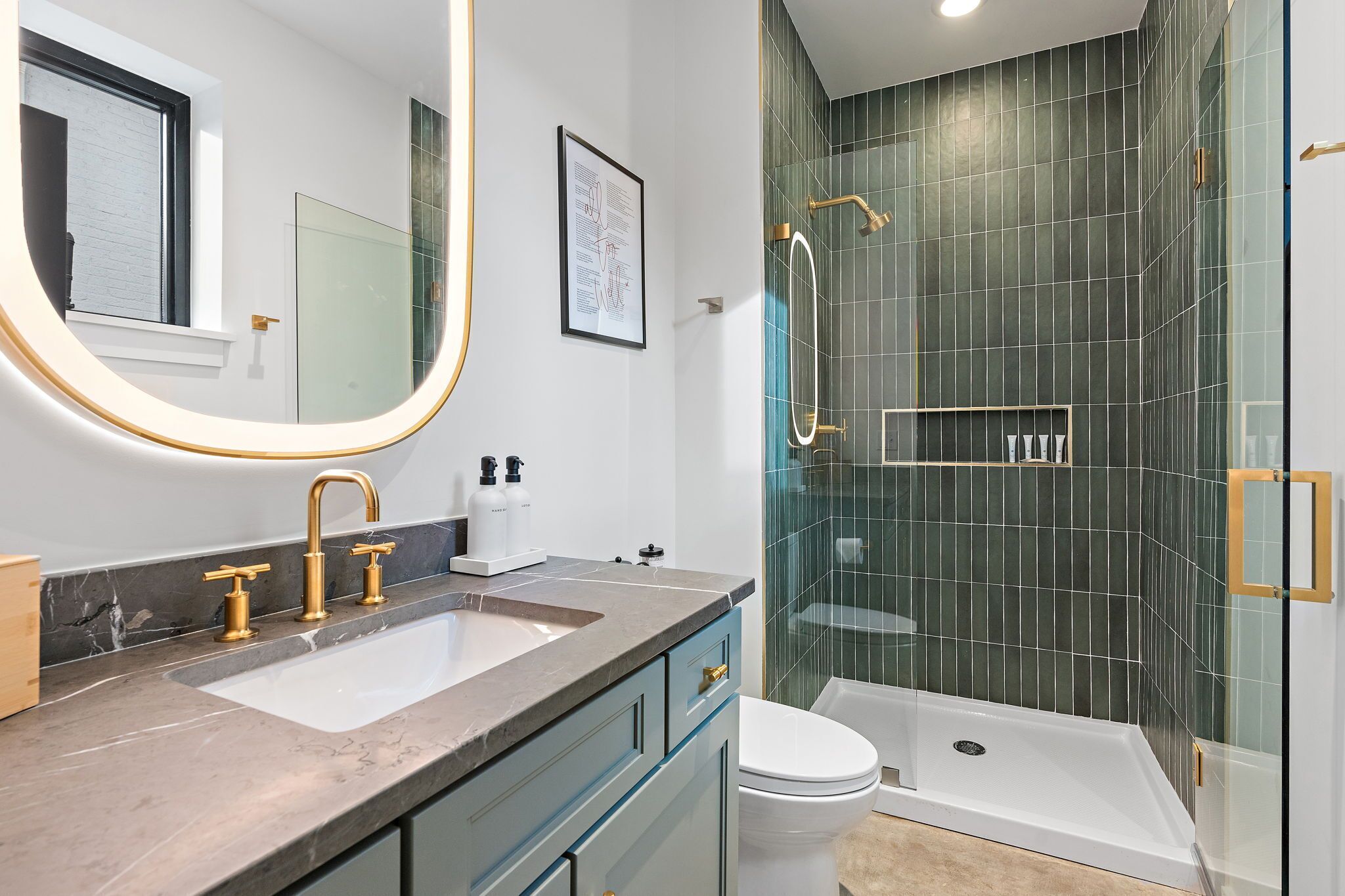 Un baño moderno con un espejo grande, un lavamanos con grifos dorados, un inodoro y una zona de ducha con paredes de vidrio.