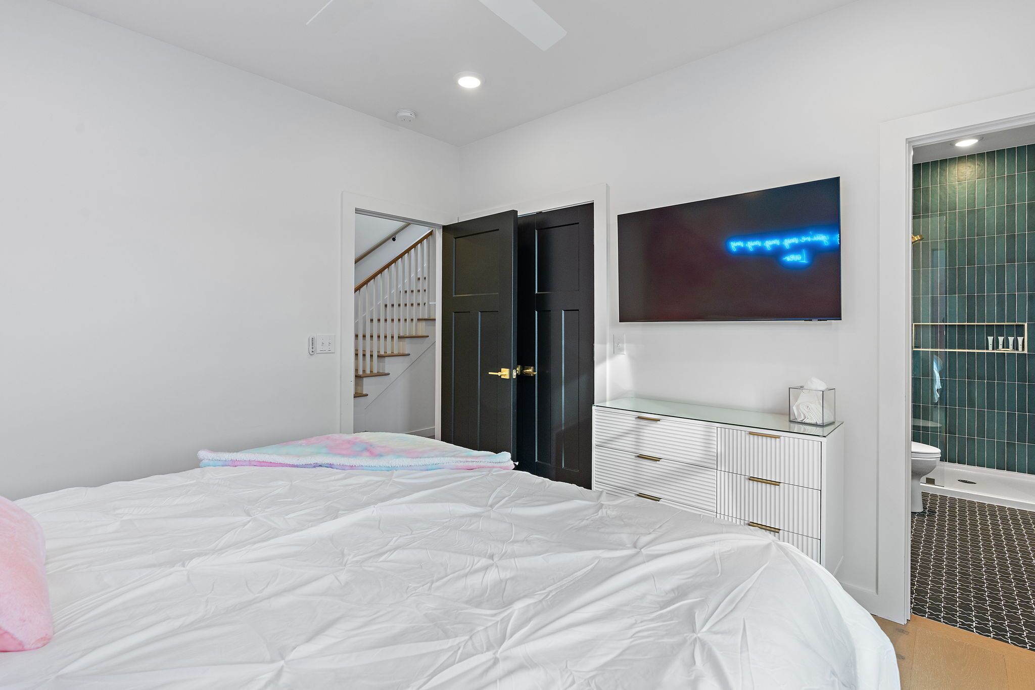 A bedroom with a bed, a dresser, a TV, and a bathroom visible through an open door.