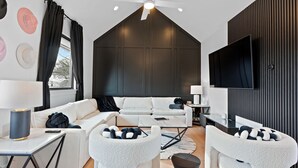A modern living room with a white sofa, a coffee table, and a TV mounted on the wall. - Music Row (Taylor's Version) Townhome (Nashville)