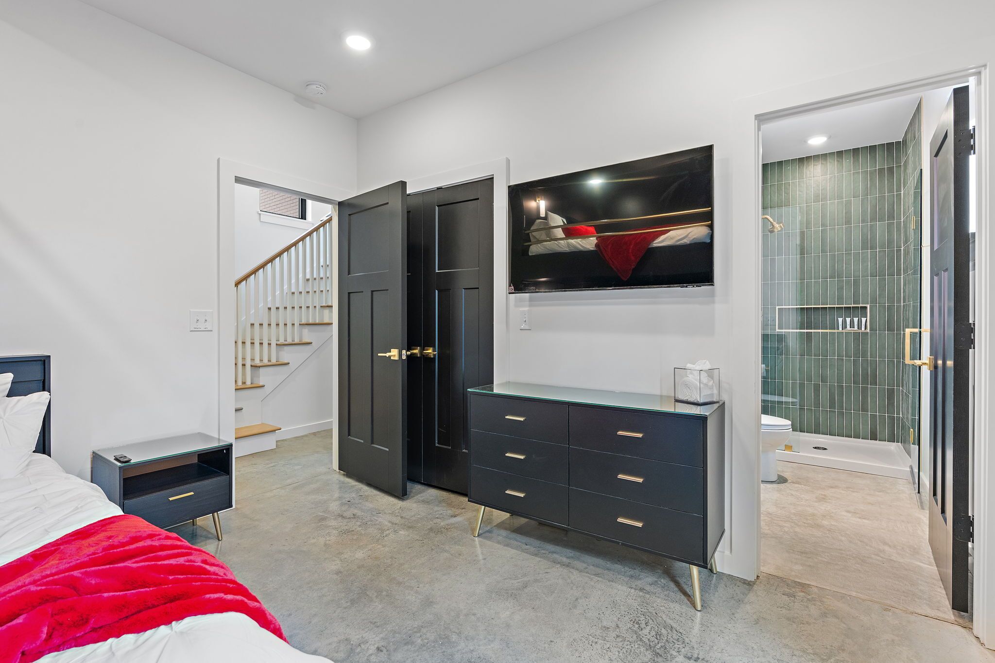 A modern bedroom with a bed, a nightstand, a dresser, a TV, and a bathroom with a shower and toilet.