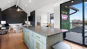 A modern kitchen with a central island, dark cabinetry, and a view of the city through a large sliding door. - Music Row (Taylor's Version) Townhome (Nashville)