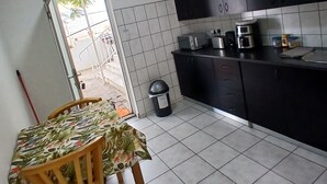 Una cocina con una mesa de comedor y sillas, un cubo de basura y una ventana con vistas al exterior.