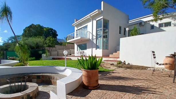 Una casa moderna con un patio de piedra, un elemento acuático circular y una planta grande en maceta.
