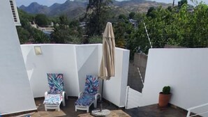 Una piscina con cubierta de baldosas, rodeada de muros blancos y vista a las montañas.