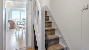 Una escalera con peldaños alfombrados que conduce a un rellano, una pared blanca y una puerta abierta que da a un cuarto con una mesa y sillas de comedor.