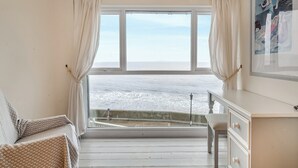 Una habitación con un gran ventanal con vista al mar, un cuadro de Picasso enmarcados y un aparador blanco.