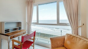 Una habitación con vistas al mar, un escritorio de madera, una silla roja y un sofá de mimbre.