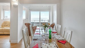 Un comedor con vistas al mar, paredes blancas y una mesa de madera dispuesta para cuatro.