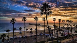 A beach with palm trees, a pier, and a parking lot. - 706 S Pacific Unit C · Steps From Beach, Panoramic Ocean Views & Parking (Oceanside)