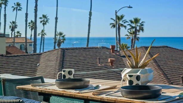 A dining table with two white mugs with black polka dots, a black bowl, and a potted plant. - 706 S Pacific Unit C · Steps From Beach, Panoramic Ocean Views & Parking (Oceanside)